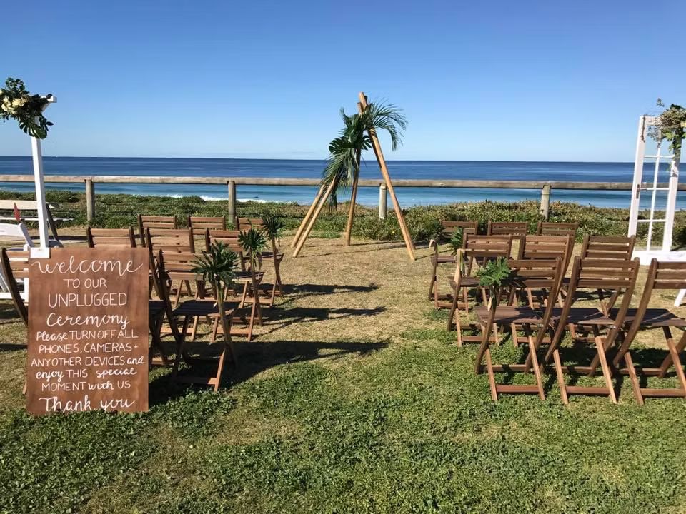 A Wedding Ceremony is Taking Place on the Beach With Wooden Chairs and a Sign ― Central Coast Events in Berkeley Vale, NSW