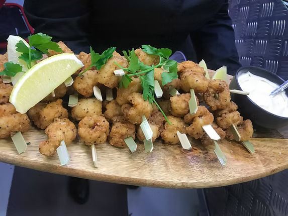 A Person is Holding a Wooden Cutting Board Topped With Fried Shrimp on Skewers ― Central Coast Events in Berkeley Vale, NSW