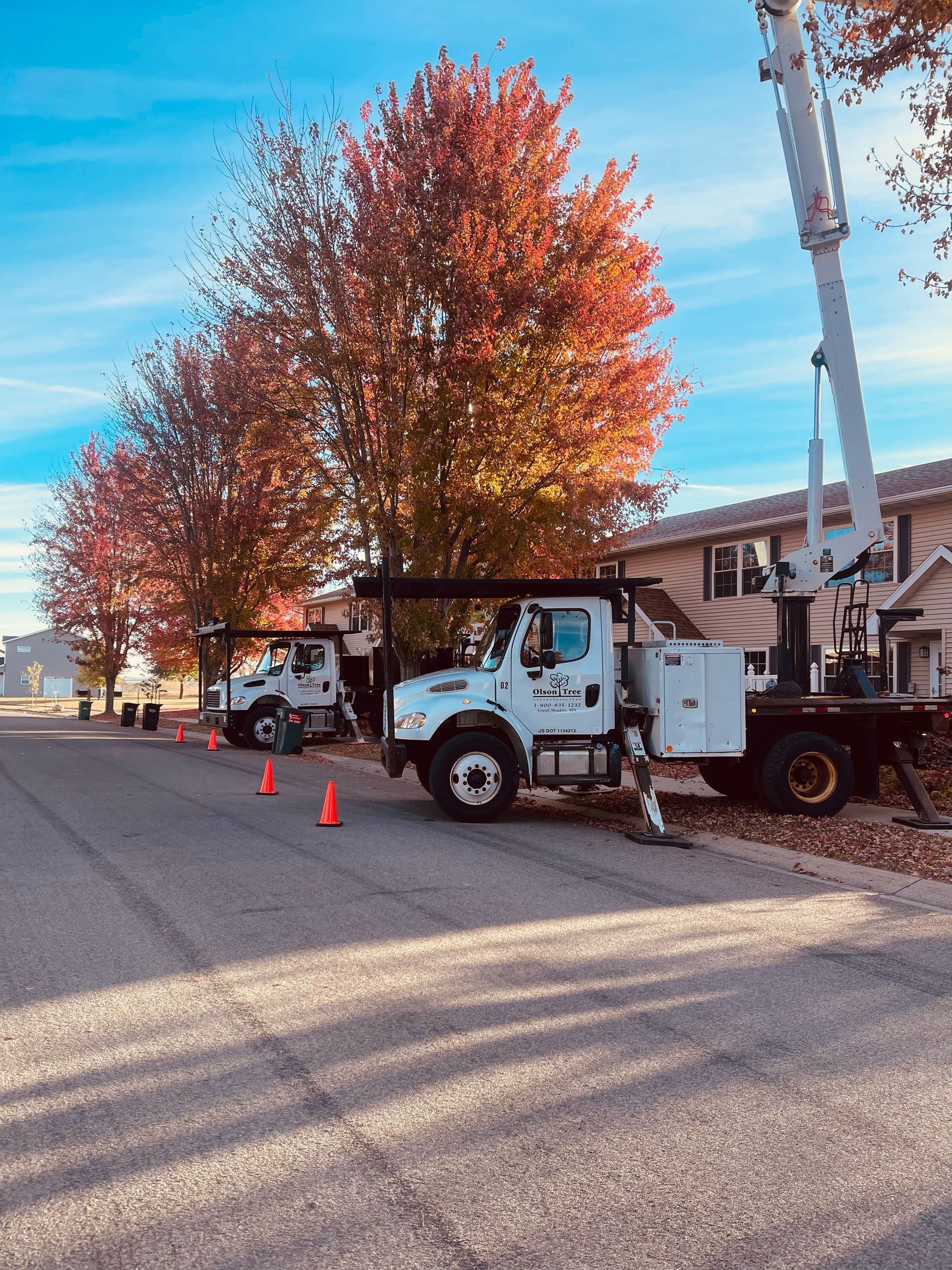 A white truck with a crane on top of it is parked on the side of the road.