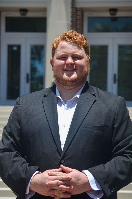 A woman is sitting at a desk with a laptop and a vase of flowers.