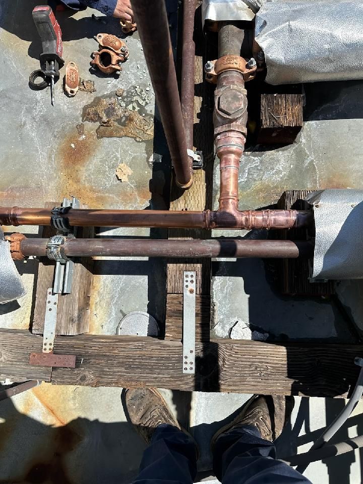 A person is standing on a wooden platform next to rusty pipes.