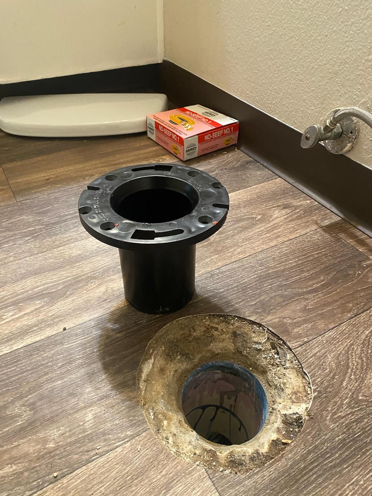 A toilet flange is sitting on the floor next to a hole in the floor.