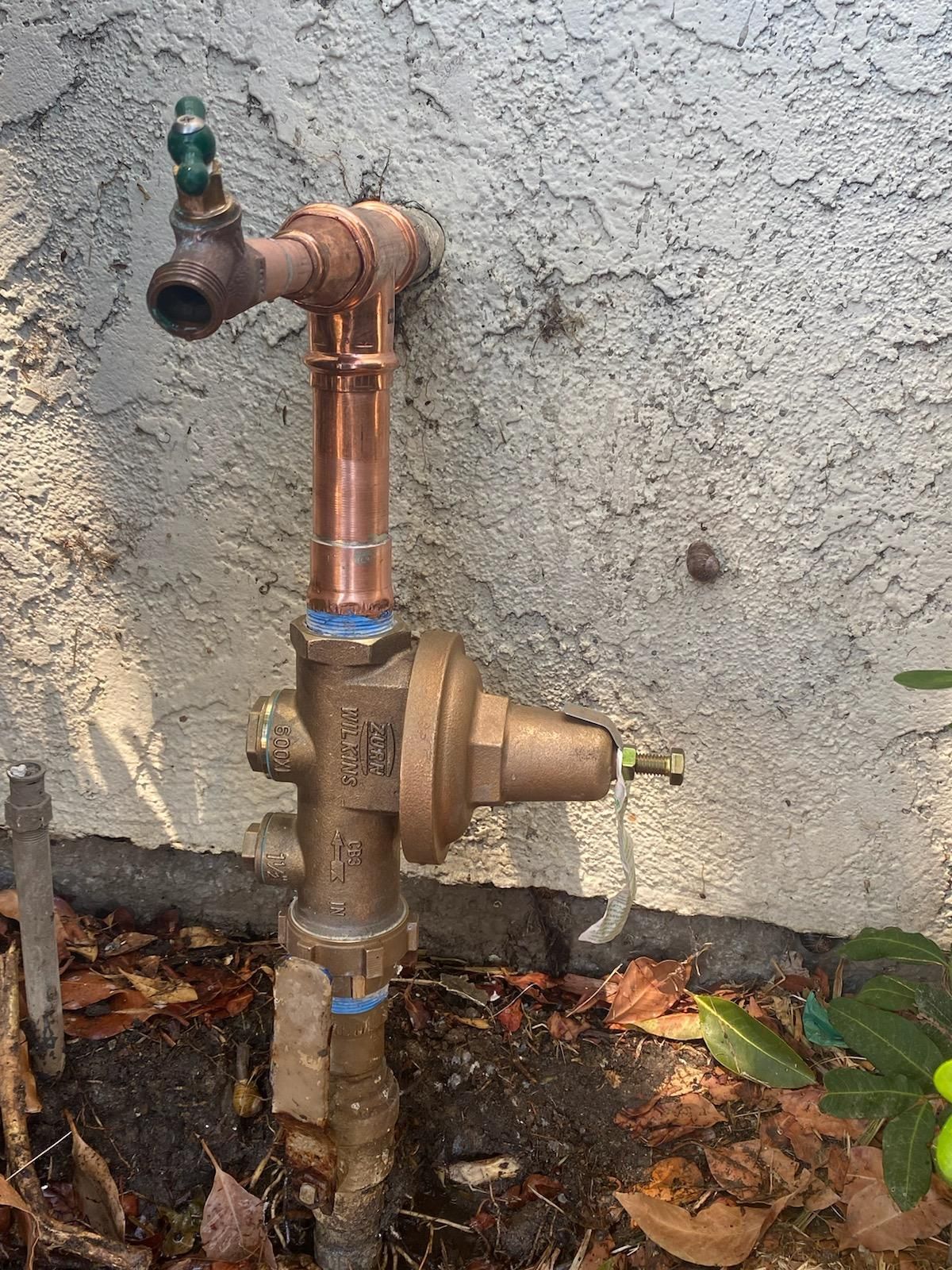 A copper pipe with a valve attached to it is sitting next to a wall.