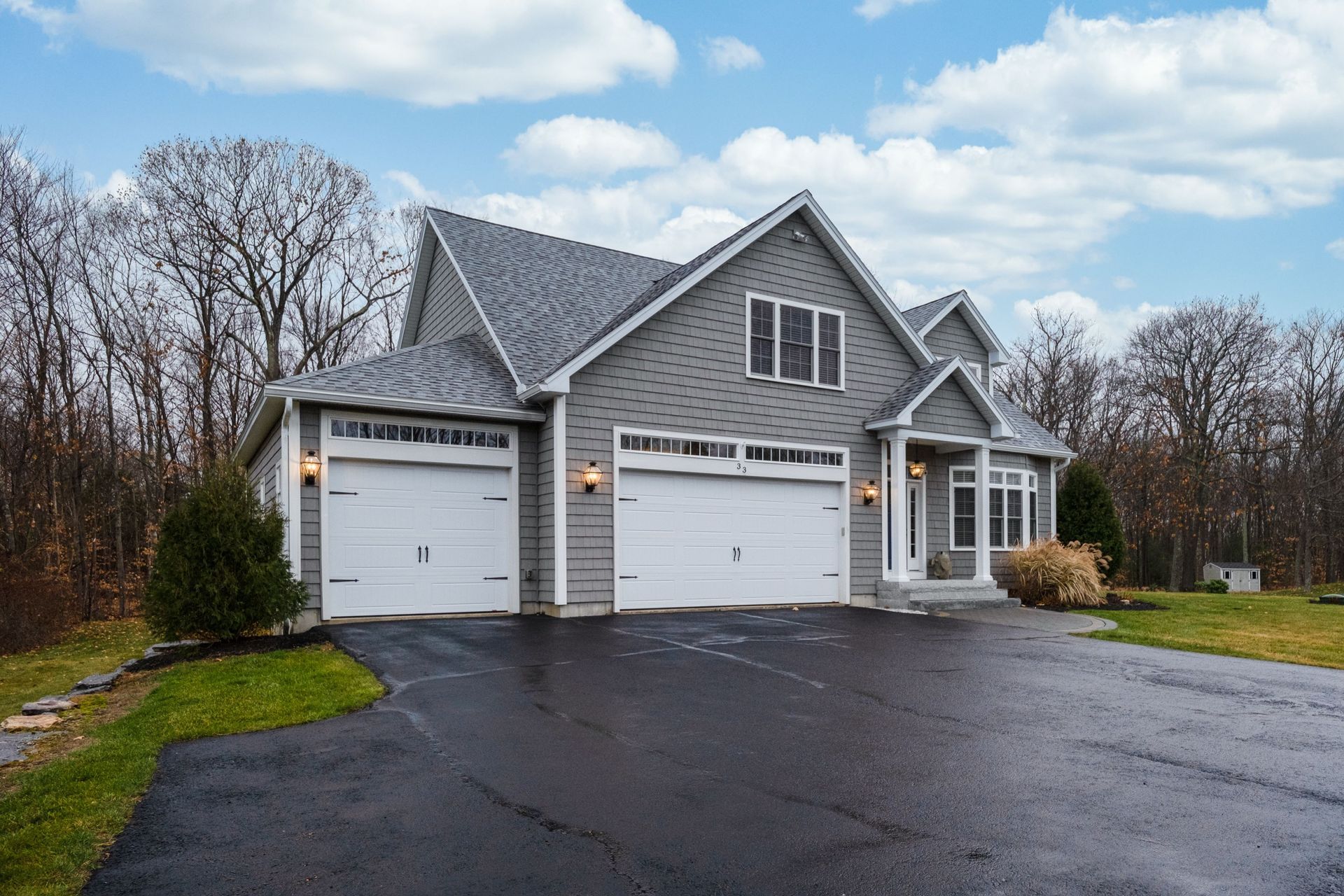 A gray-walled suburban residential property with white garage doors and newly driveway paving.