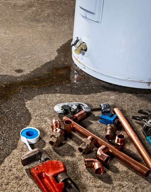 A water heater is sitting on the ground next to a bunch of pipes and tools.