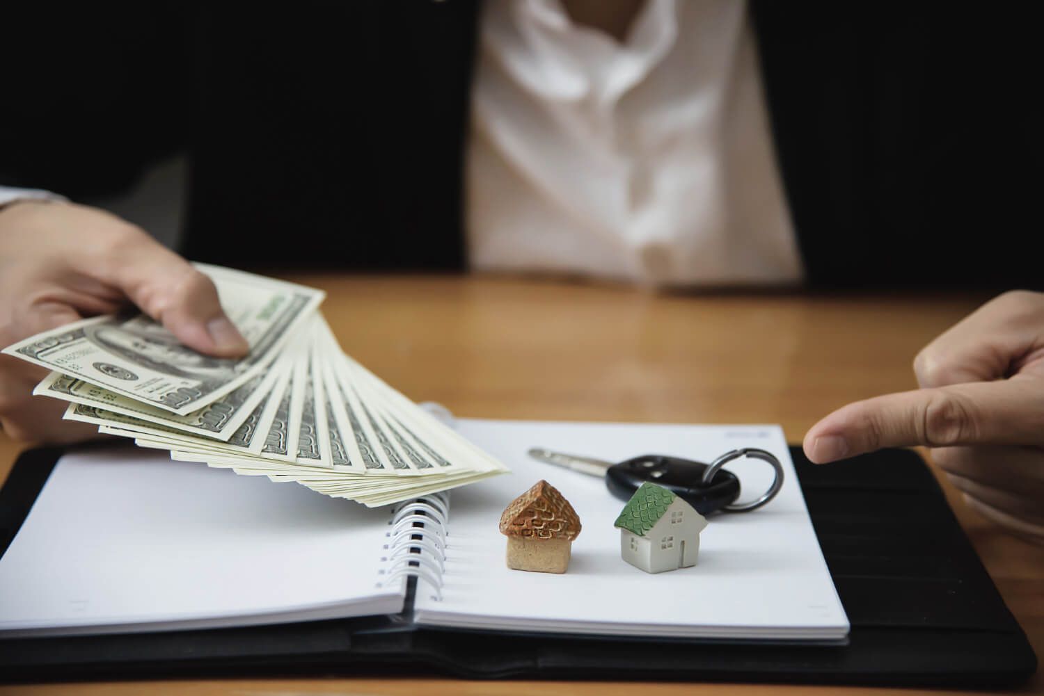 A person is holding a bunch of money over a notebook.