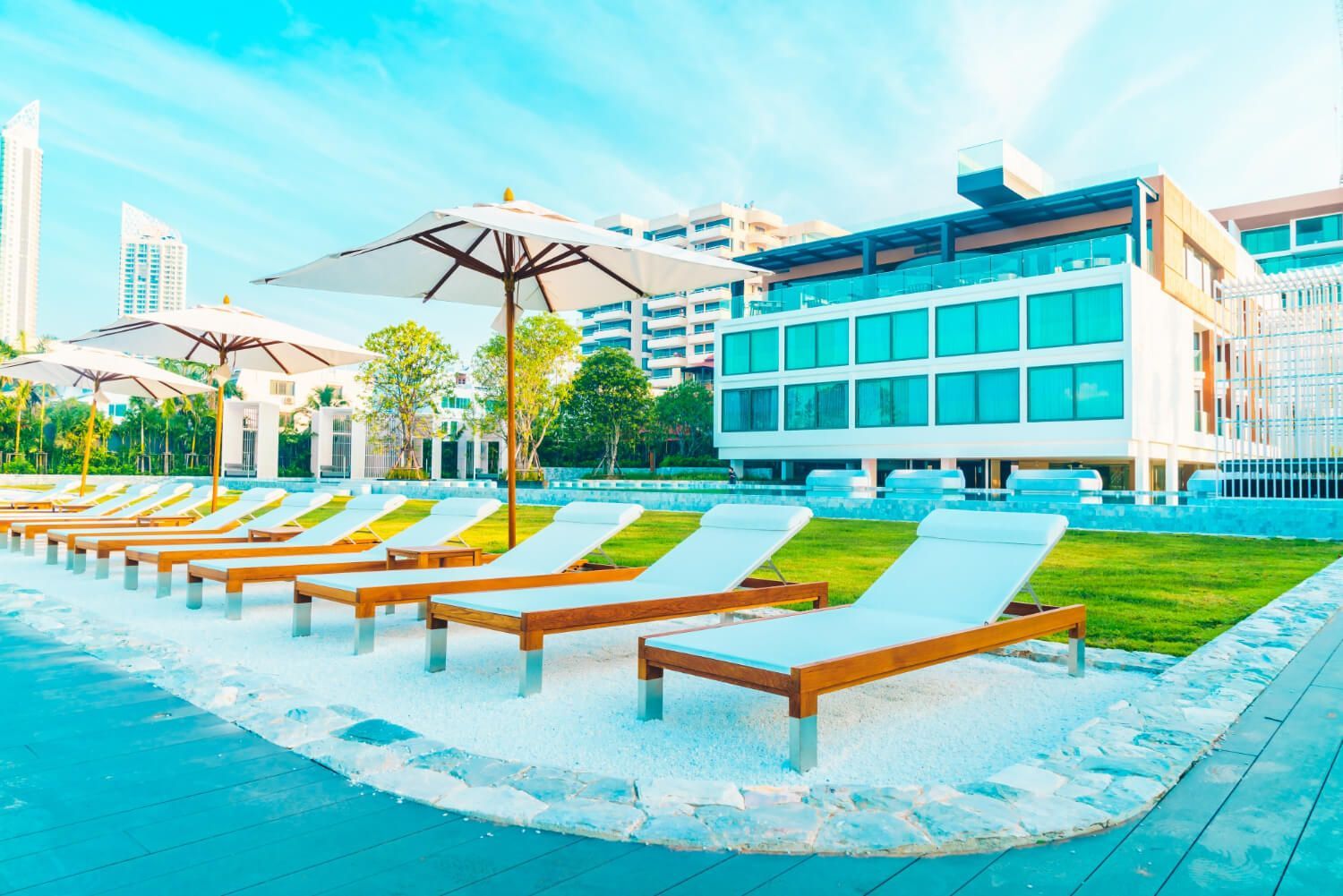 A row of lounge chairs and umbrellas next to a swimming pool.