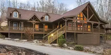 A large log cabin is sitting on top of a hill in the woods.