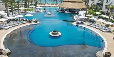 A large swimming pool surrounded by chairs and umbrellas in a resort.