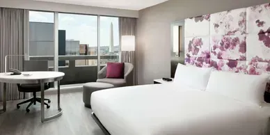 A hotel room with a king size bed , desk , chair and balcony.