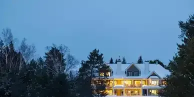 A large house is surrounded by snow and trees at night.