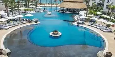 A large swimming pool surrounded by chairs and umbrellas in a resort.