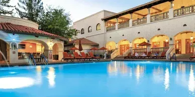 A large swimming pool surrounded by chairs and umbrellas in front of a building.