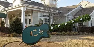 A statue of a guitar is in front of a house.