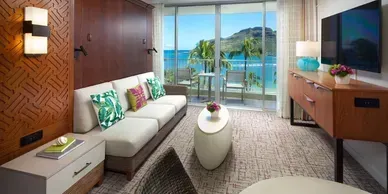A living room with a couch , table , television and a view of the ocean.