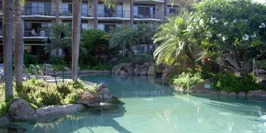 A large swimming pool surrounded by palm trees in front of a building.