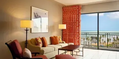 A living room with a couch , chairs , lamps and a balcony overlooking the ocean.
