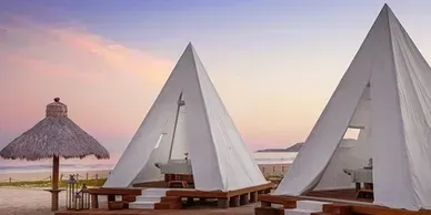 A row of white tents on a beach with umbrellas.