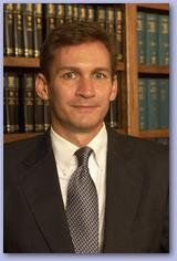 A man in a suit and tie is standing in front of a bookshelf.