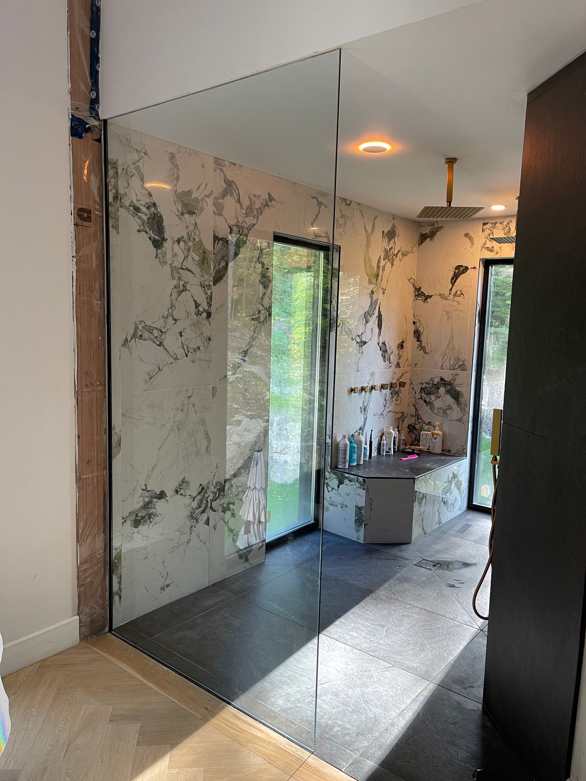 Une salle de bain partiellement construite avec un grand miroir, des murs en marbre et un sol gris.