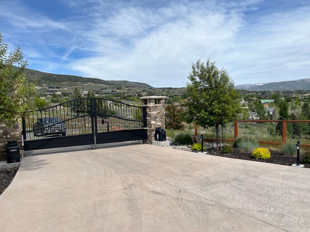 A driveway with a gate leading to a house with mountains in the background.