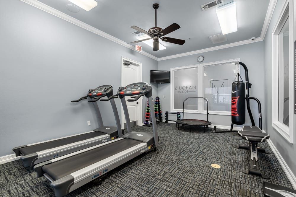 A gym with treadmills , a boxing bag , and a ceiling fan at Marquis Rockwall in Rockwall, TX.