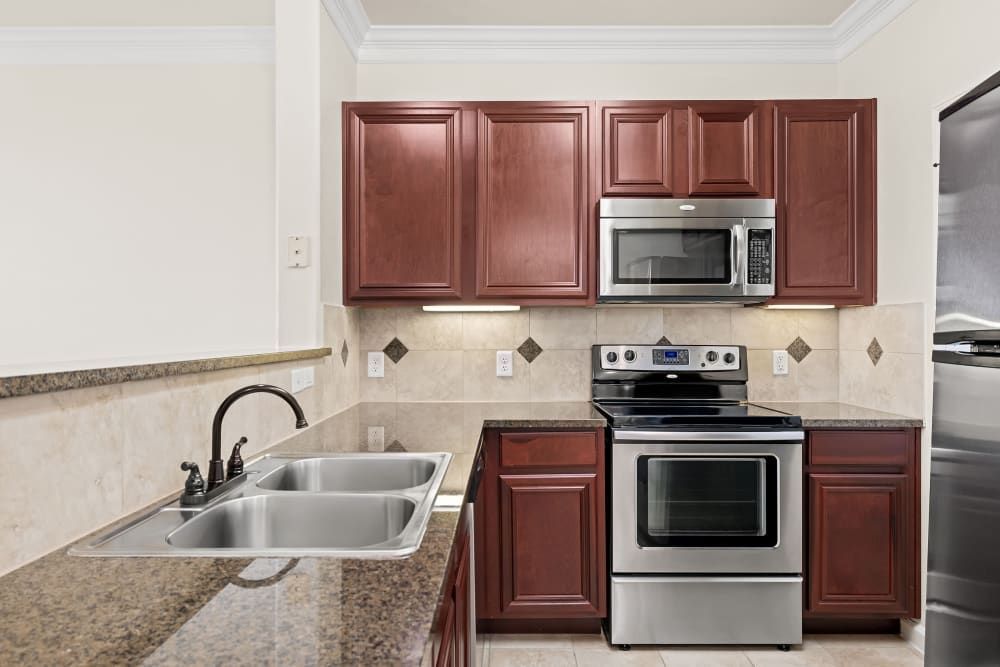 Apartment  kitchen with double sink, stainless steel appliances and wooden cabinets at Marquis Rockwall in Rockwall, TX.