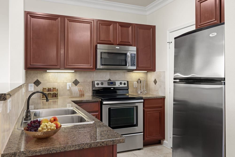 Apartment kitchen with stainless steel appliances and wooden cabinets at Marquis Rockwall in Rockwall, TX.