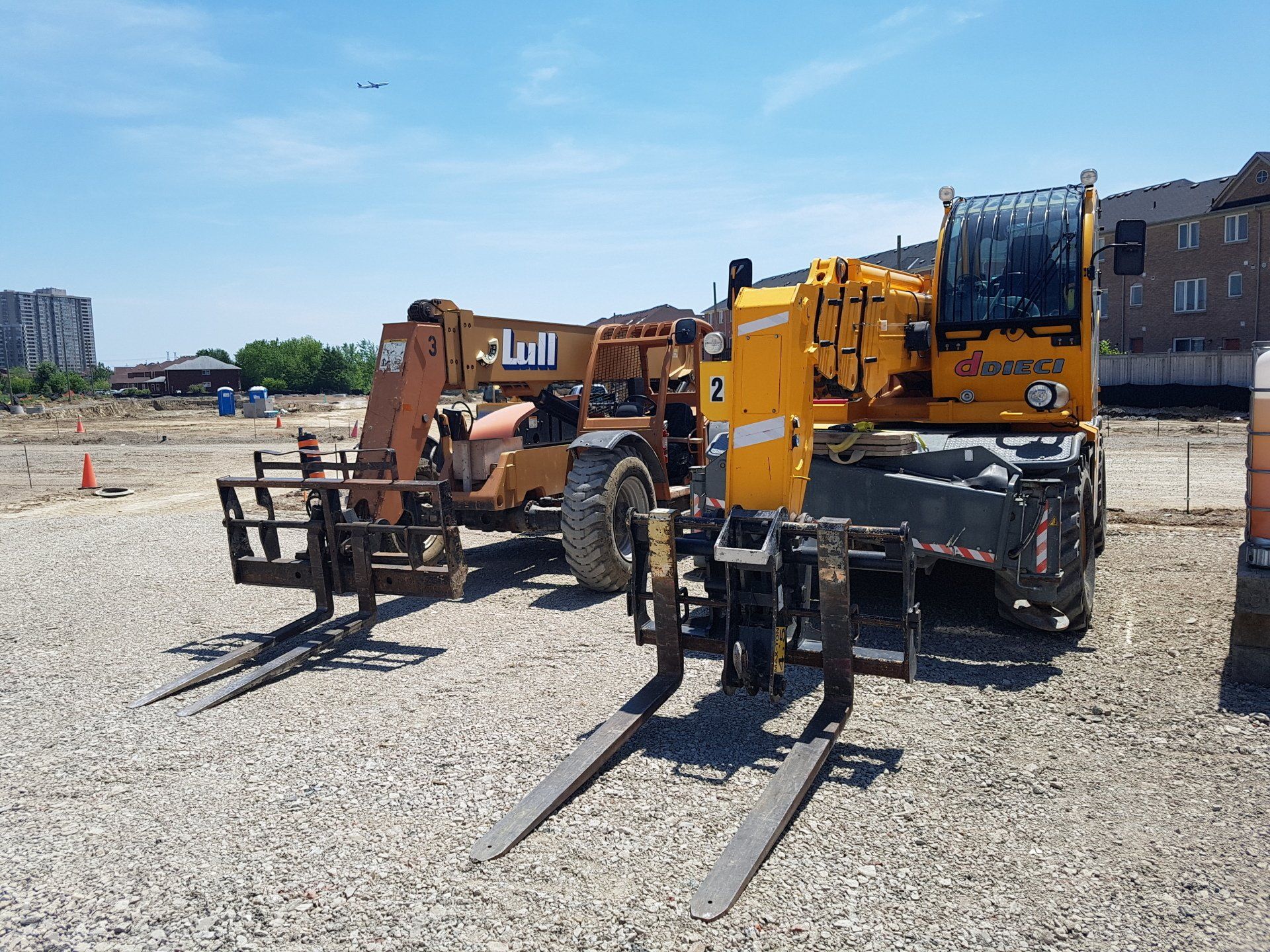 Two forklifts are parked next to each other in a gravel lot.