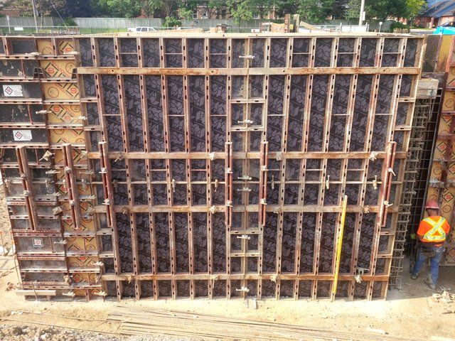 A man in an orange vest is standing in front of a wall that is being built.