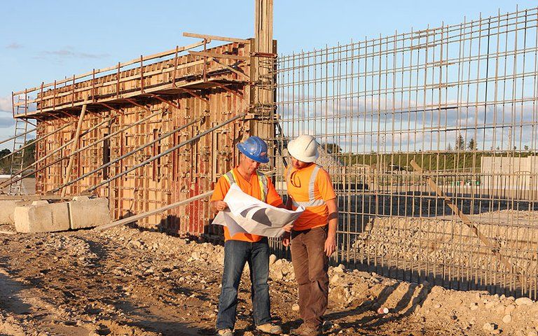 Two construction workers are looking at a blueprint on a construction site.