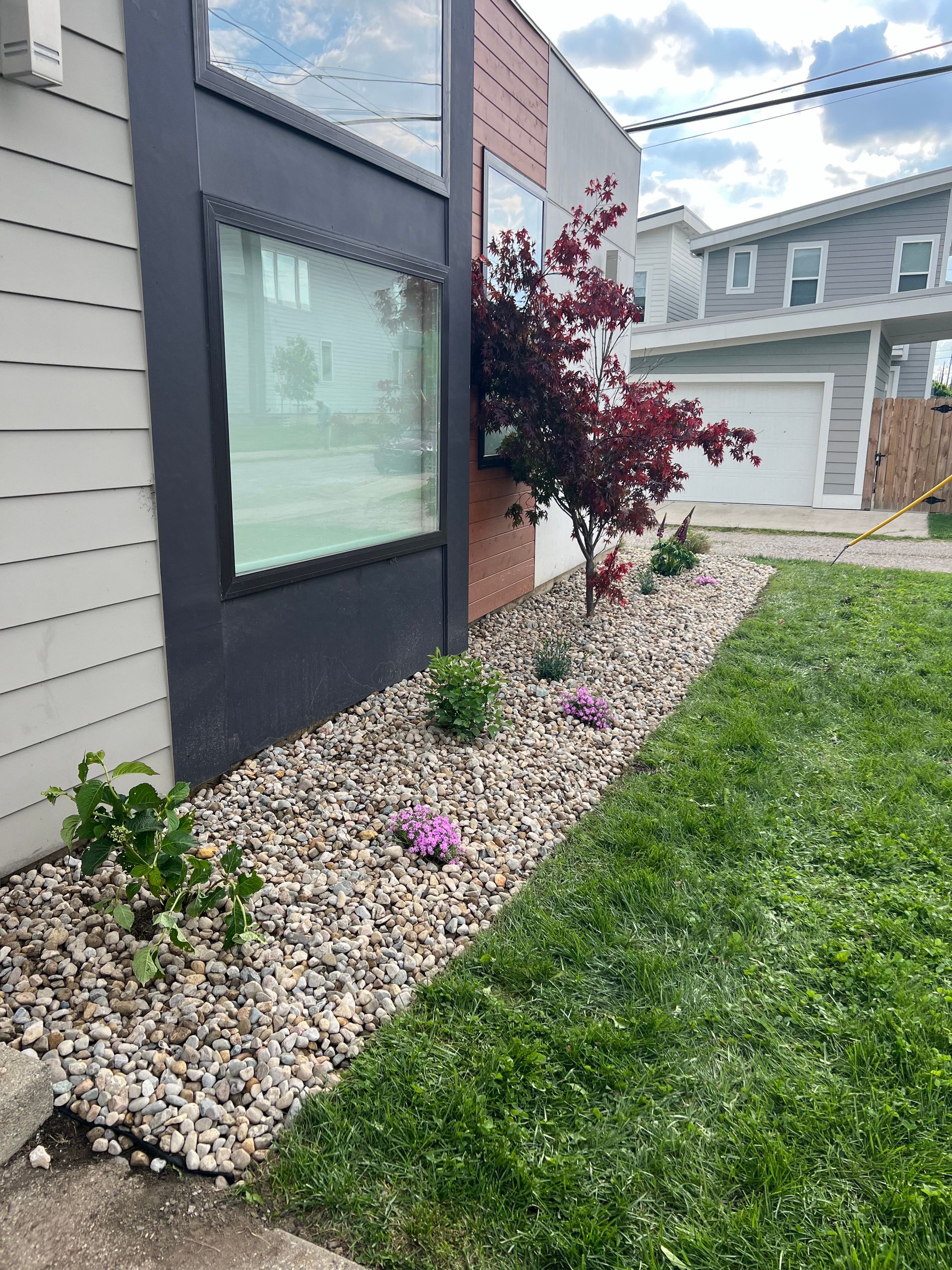 A yard with a lot of rocks and plants in front of a house.