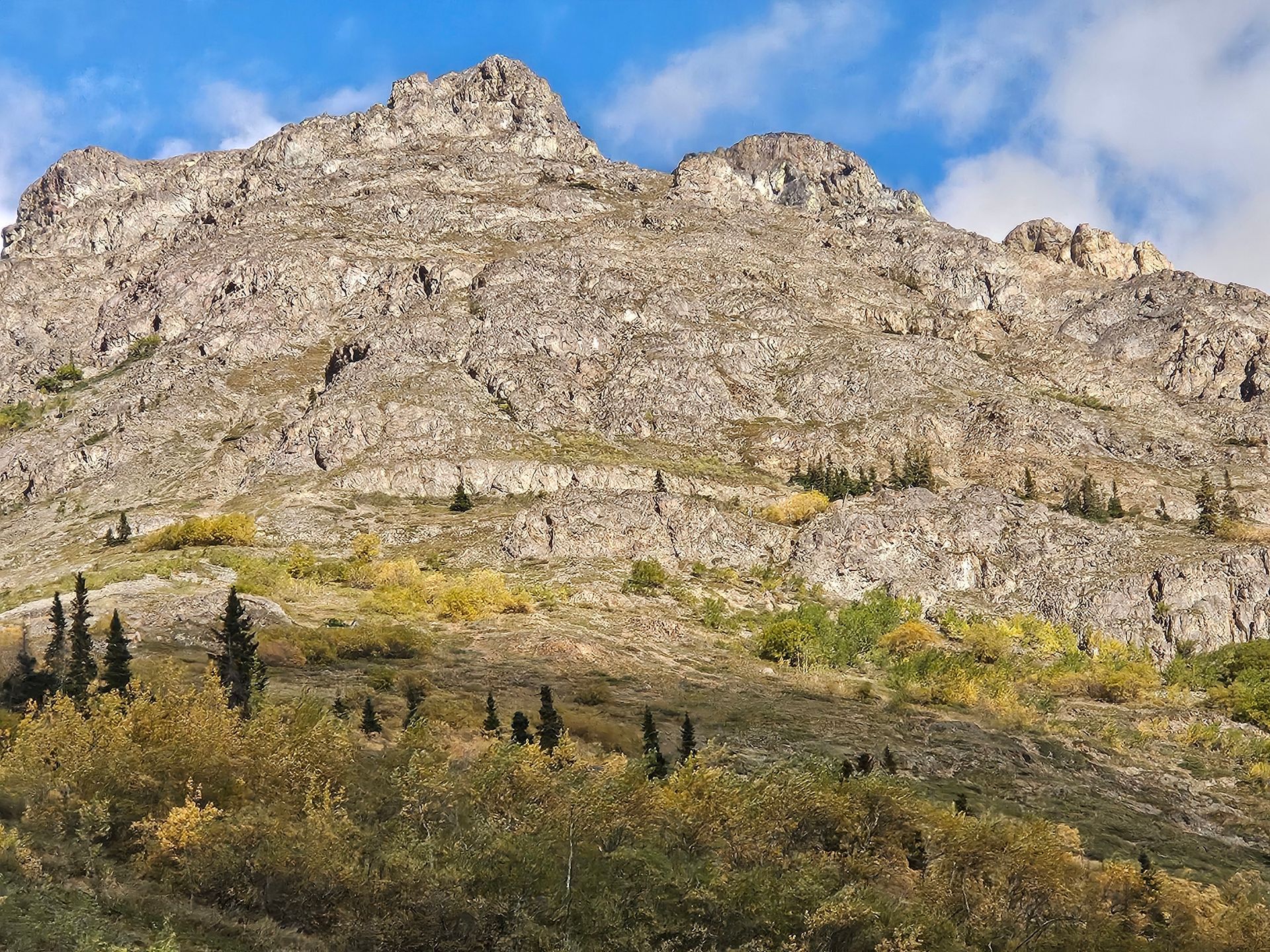 Rocky mountain with sparse vegetation and a blue sky.