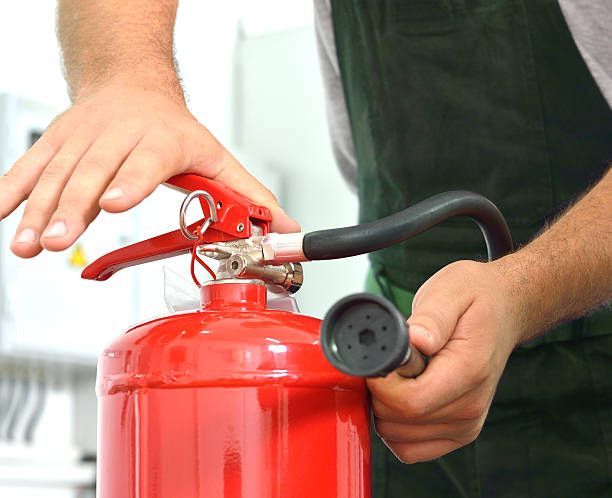 Technician inspecting red fire extinguisher and testing nozzle during safety maintenance service.