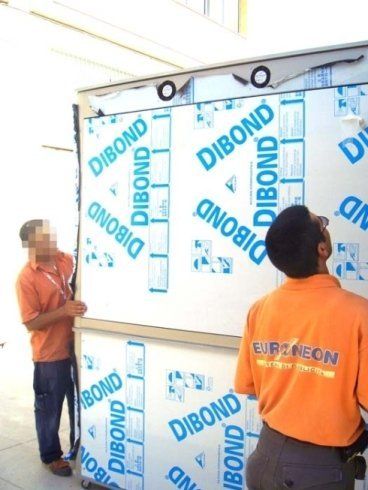 Due uomini installano pannelli Dibond su una struttura, uno dei quali guarda verso l'alto.