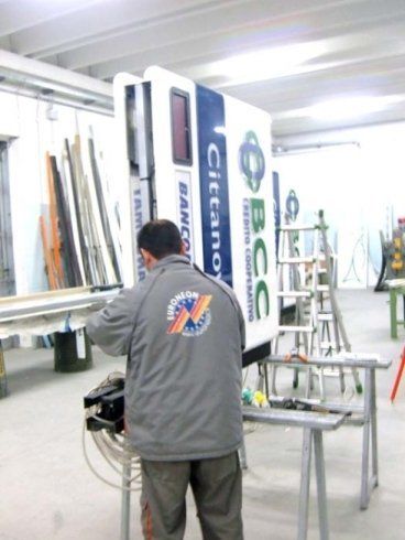 Un uomo che lavora su un grande cartello bianco con dei loghi, probabilmente in un'officina.