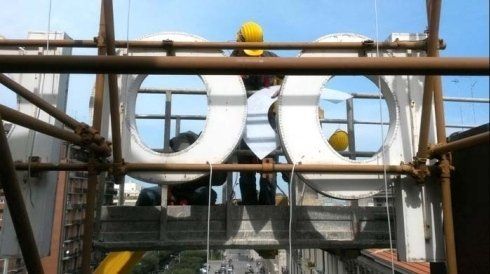 Operai edili su impalcature vicino a grandi strutture circolari bianche; sullo sfondo della città.