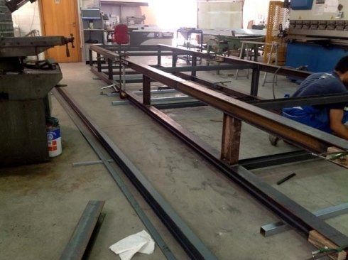 Lavoratori metalmeccanici costruiscono una struttura in acciaio in un'officina; una persona salda.