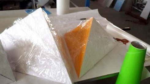 Pezzi triangolari bianchi e arancioni con pellicola trasparente e un tubo verde su un tavolo.