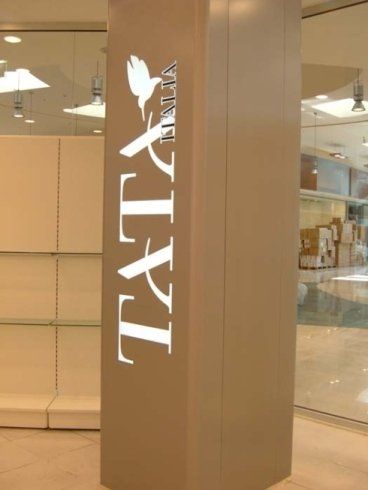 Insegna di TATY Italia su un pilastro beige in un centro commerciale, con il logo di una colomba bianca.