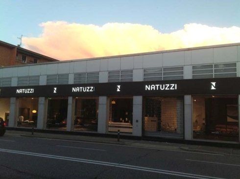 Negozio di mobili Natuzzi con insegna nera e logo illuminato sotto un tramonto colorato.