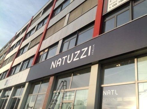 Esterno del negozio Natuzzi Italia; grande insegna grigia sull'edificio, vetrine, dettagli rossi.