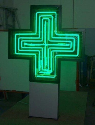 Insegna al neon verde a forma di croce per farmacia su base bianca.