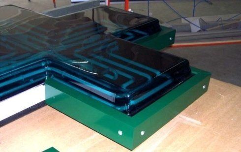 Insegna verde a forma di croce per farmacia, primo piano. Piano in vetro scuro con linee interne color verde acqua. Base verde brillante.