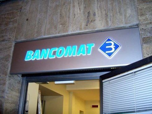 Un cartello con la scritta Bancomat, un bancomat, sopra un portone. Il testo è azzurro su sfondo marrone.