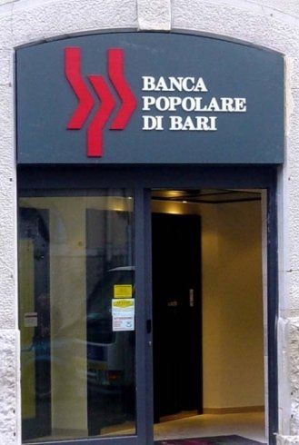 Ingresso della Banca Popolare di Bari con logo rosso su cartello grigio scuro sopra le porte in vetro.