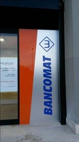 Ingresso di un Bancomat con insegna arancione e argento, testo e logo blu.