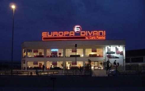 Negozio Europa Divani di notte, insegna al neon illuminata, edificio bianco, mobili visibili attraverso le vetrine.