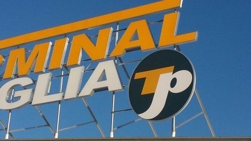 Cartello per Terminal Taglia, lettere gialle e bianche con logo circolare, sullo sfondo del cielo azzurro.