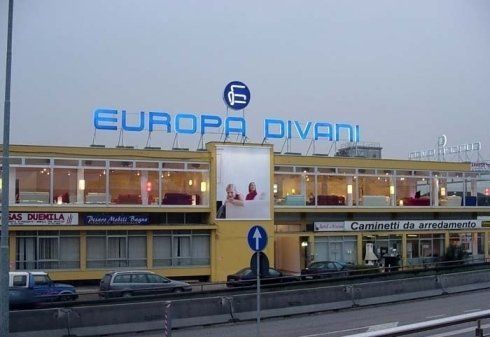 Esterno giallo del negozio Europa Divani, insegna blu, auto parcheggiate, cielo nuvoloso.